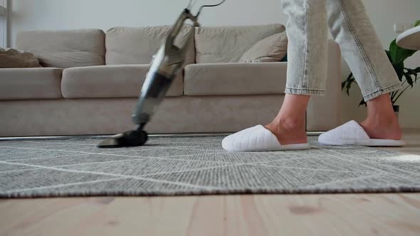 Young Woman Legs in Sneakers Cleaning Carpet with Vertical Vacuum Cleaner While Cleaning the House alt