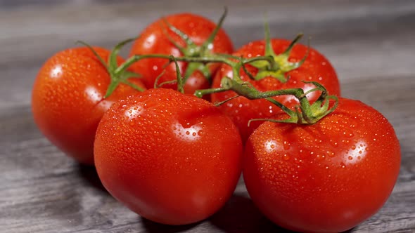 Appetizing Red Juicy Tomatoes on a Branch with Water Drops Lie on a Wooden Surface and Spin alt