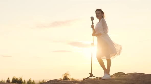 Beautiful Woman in White Dress on Top of Mountain on Edge of Abyss and Sings Song Into Shiny Retro alt