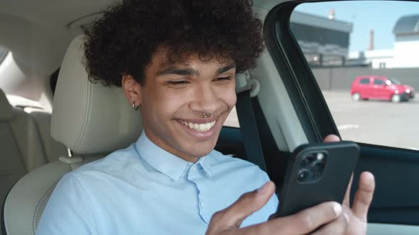 Young Business Guy of Ethnicity Scrolls the News Feed on the Smartphone While Sitting in the Car alt