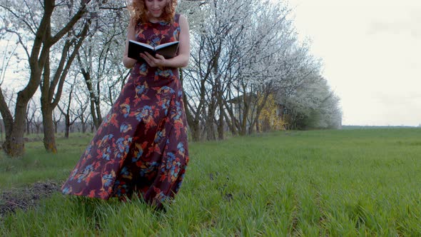 Girl in Dress Standing Turns the Page Diary on Windy Green Field alt