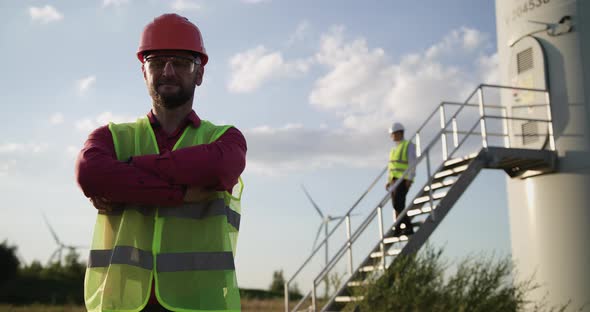 One Engineer Puts His Hand on His Hand, Looking at the Camera. In the Background, a Second Engineer alt
