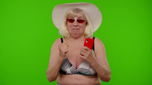Senior Woman Tourist in Sunglasses with Mobile Phone Celebrating Winning Holiday Resort Vacation alt