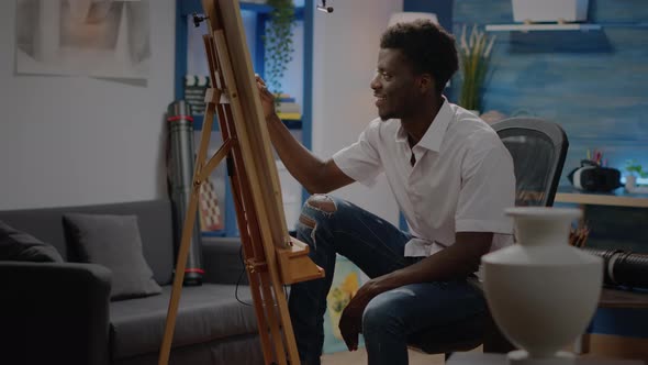 Black Young Adult Sitting in Artwork Studio Drawing Vase alt