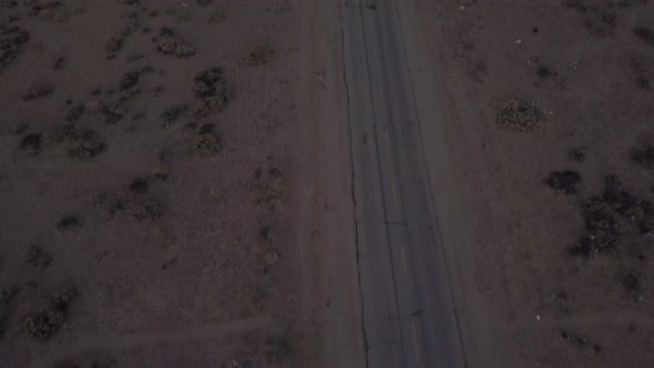 AERIAL: Birds View of Lonely Abandoned Desert Road with Red Car Driving in the Distance  alt