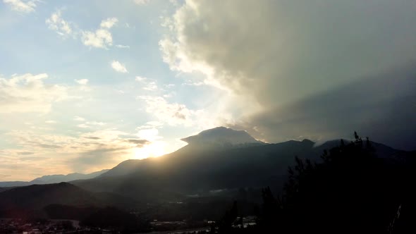 Time lapse panorama of green valley, snowy mountain and sun beams breaking through the clouds