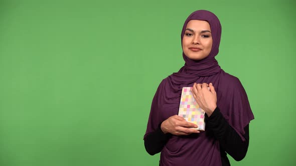 A Young Beautiful Muslim Woman Holds a Book in Her Arms and Smiles at the Camera  Green Screen