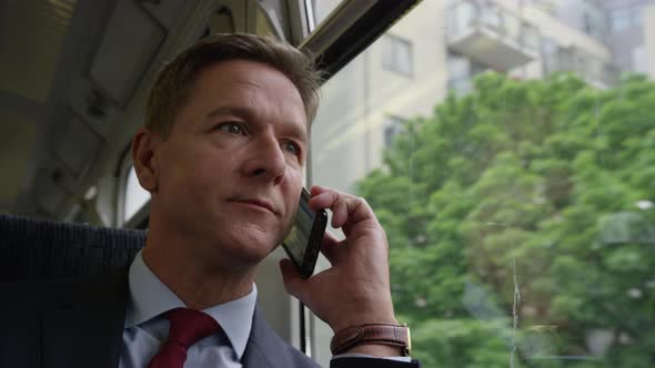 Businessman on train on his commute talking on smart phone