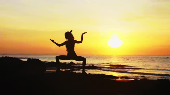 Young Woman's Silhouette Is Making Yoga Exercises on the Ocean Beach at Sunset. alt
