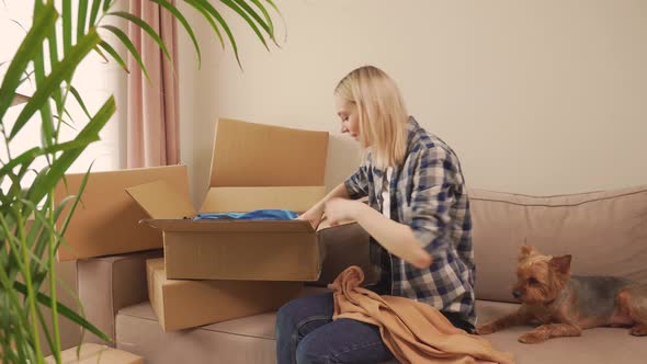 A Woman Sitting on Sofa Opens a Box of Clothes After Moving in