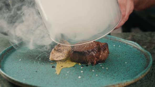 Male Hand Lifts To Up Glass Cloche From a Plate with Hot Food Beef Steak and Moving Smoke at the alt