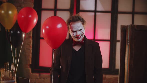 A Smiling Scary Clown in the Brown Jacket Holding a Red Balloon alt