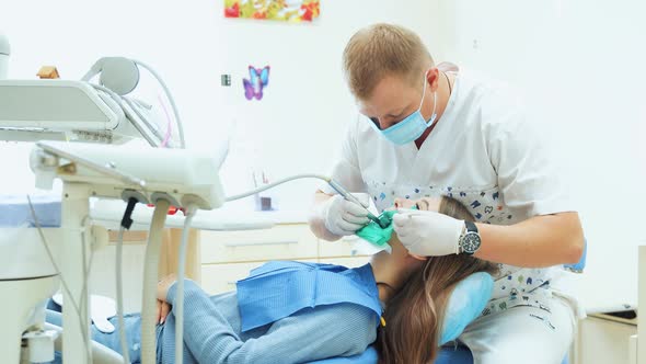 A male dentist treats a tooth with a drill to a patient. alt