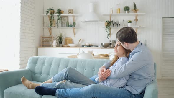 Slow Motion of Man Hugs Lady Sitting on Sofa and Kissing in Kitchen alt