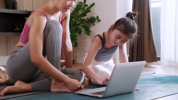 Attractive Asian woman and girl practicing yoga exercise online course with laptop at home