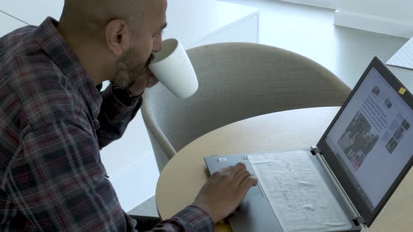 Asian Businessman Checking News and Financial Statements on Laptop with Morning Coffee alt
