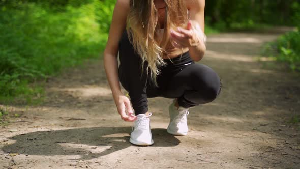 A Woman Ties Her Shoelaces While Running Through the Woods alt