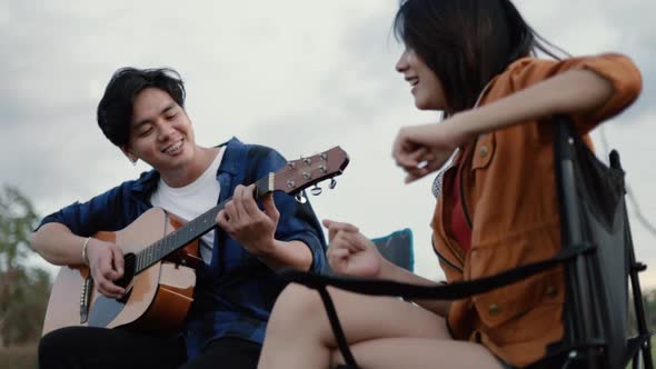 A happy young Asian couple backpacker playing the guitar and singing a song together.