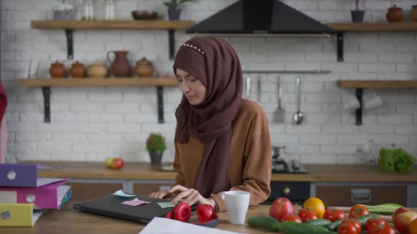 Confident Beautiful Woman in Hijab Drinking Morning Coffee Opening Laptop Putting on Headphones in alt