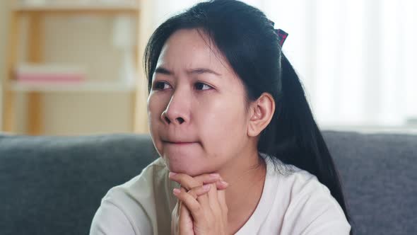 Depressed crying Asian business woman stressed with headache sitting on sofa in living room. alt