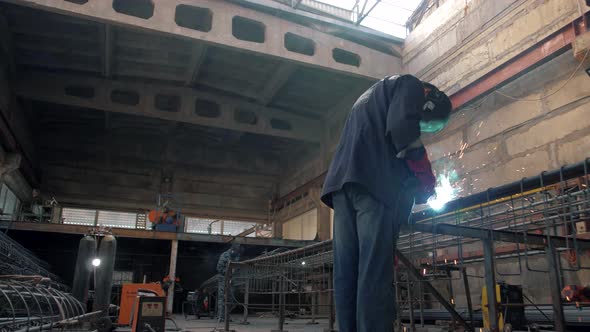 Factory workers in a huge workshop welds metal structures alt