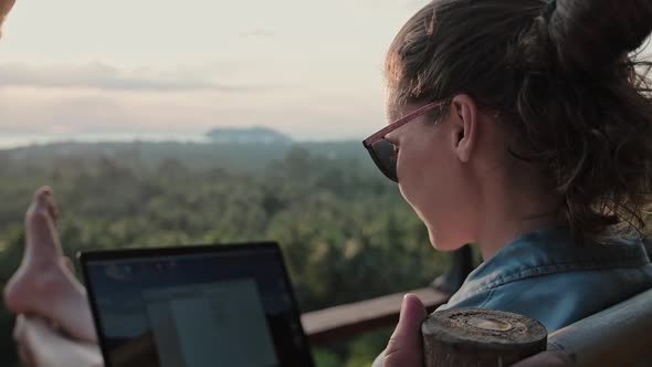 Freelancer woman sits with a laptop on a high bar chair.  alt