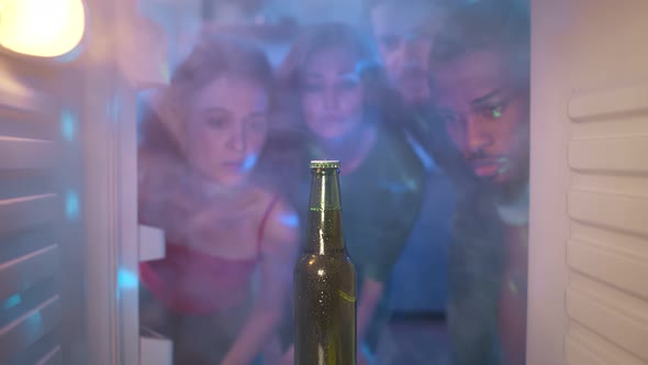 Sad Diverse Friends Look at Last Beer Bottle in Fridge alt