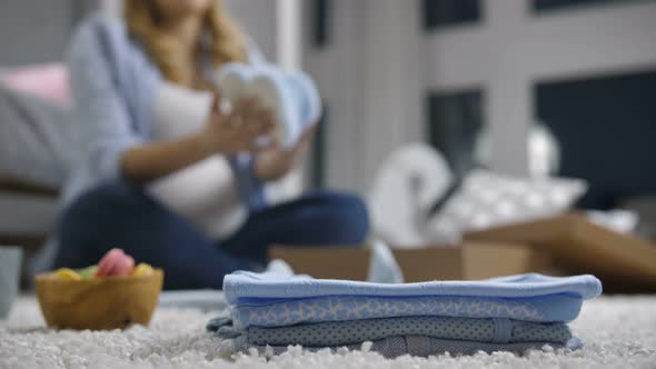 Pile of Baby Clothes with Defocused Pregnant Woman alt