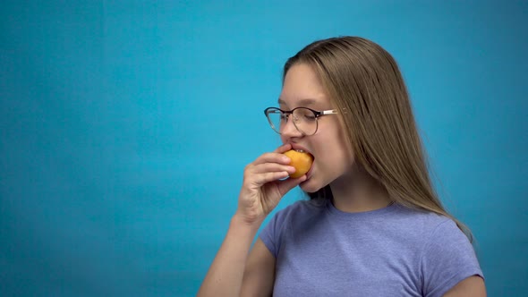 Teenager Girl with Braces on Her Teeth Eats an Apricot on a Blue Background. Girl with Colored alt