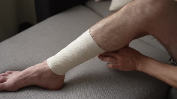 Man is Bandaging His Leg with an Elastic Bandage alt