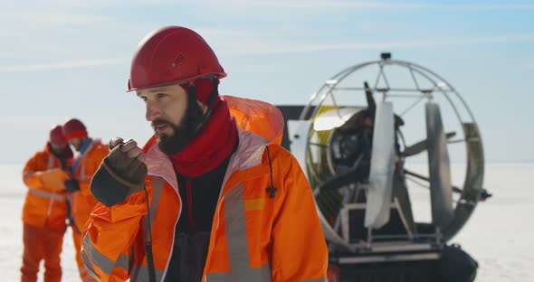 Male Rescuer in Orange Uniform Talking on Walkietalkie Standing on Frozen Lake alt