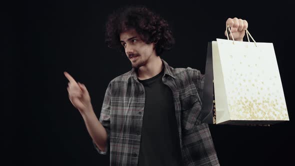 The Charismatic Handsome Young Man Holds Two Packages in His Hand with the Other Hand Points to One alt