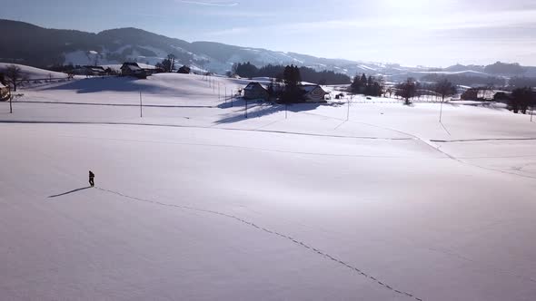 Young man walks through a big snowy field in the winter in Switzerland. alt