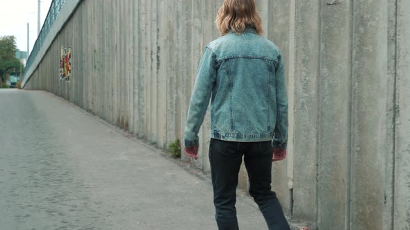 Fashionable young attractive man with blue eyes, long blond curly hair in blue denim jacket walking