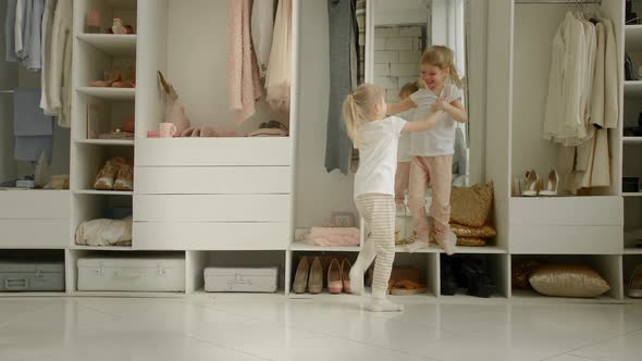 Twin Girls in Pajamas Play Against the Background of the Wardrobe