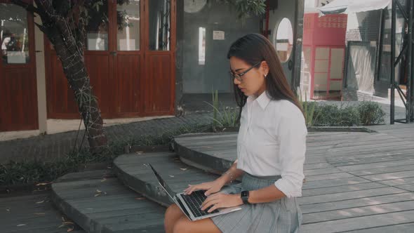 Asian Attractive Young Woman Wearing Glasses Working at Her Laptop on the Street alt