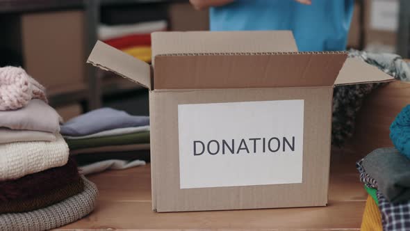 Female Volunteer Sorting Clothes and Putting It Into the Cupboard Box at the Warehouse alt