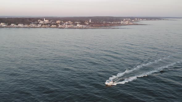 Fishing boat heading out at sunrise with two lighthouses in the distance AERIAL Orbit alt