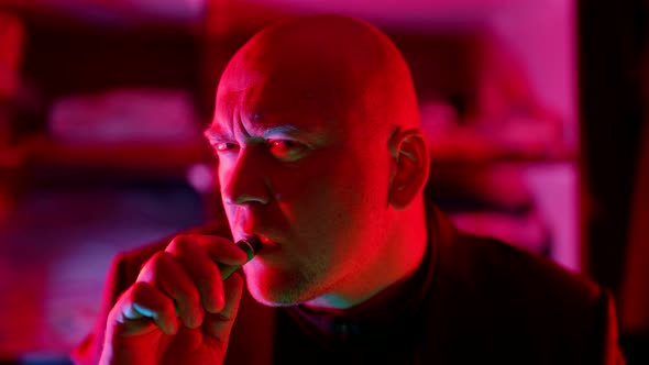 a Bald Man Looks Frowningly at the Camera Then Takes a Drag on an Electronic Cigarette in a Flashing alt