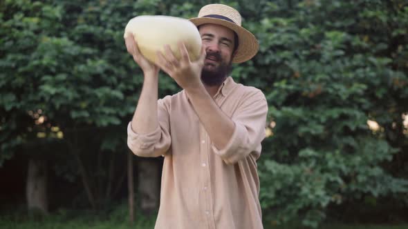 Medium Shot Portrait of Smiling Satisfied Male Farmer Juggling Big Zucchini Showing Thumb Up Looking alt