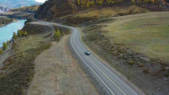 Blue Car Drives Along the Road in the Mountains Along the River alt