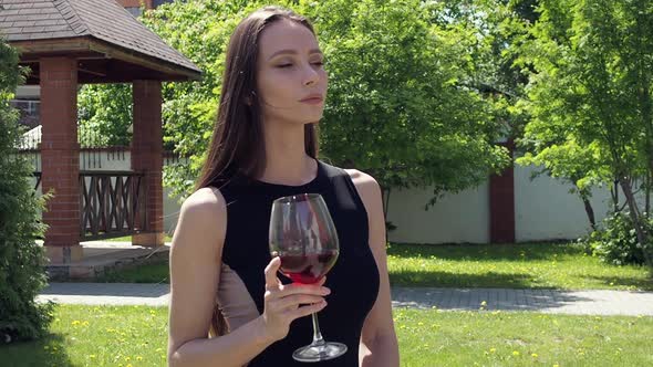 Elegant Woman with Glass of Wine Walking in Garden of Mansion