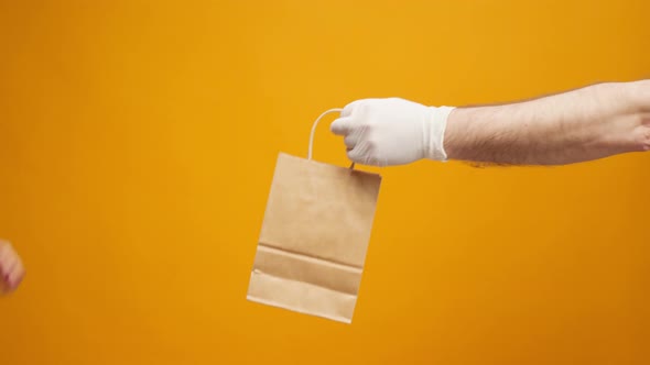 Courier in Gloves Passing Craft Shopping Bag with Delivery Against Yellow Background alt