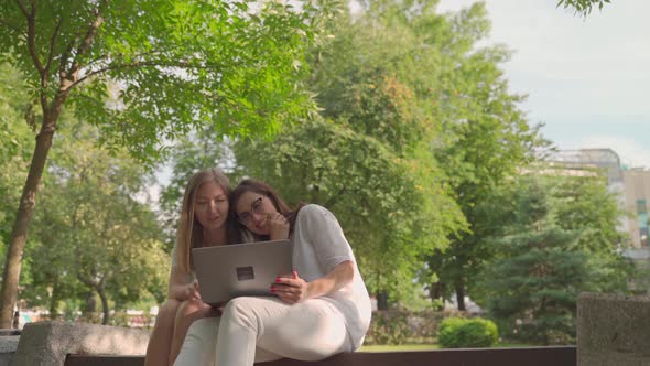 Young Woman Helping Her Old Retired Mother on a Laptop Sitting in a Park. Concept of Age Inclusivity alt