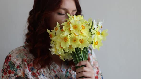 Portrait of Young Romantic Woman Smelling Spring Yellow Daffodils Flowers in Bouquet at Home