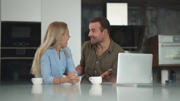 Happy Excited Couple Cheering Satisfied with Results on Laptop Drinking Coffee in Kitchen alt
