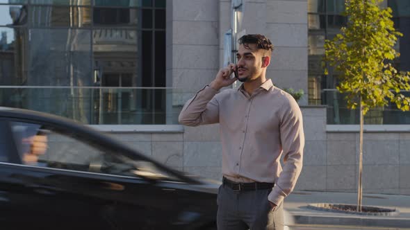 Hispanic Business Man Arabic Guy Stands on Street Background of City Buildings Talking on Mobile alt