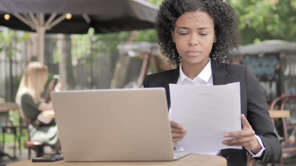 African Businesswoman Reading Documents While Sitting in Outdoor Cafe alt