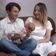 Portrait of Happy Couple Sitting on Couch with Newborn Baby Admiring Child and Looking at Camera - VideoHive Item for Sale