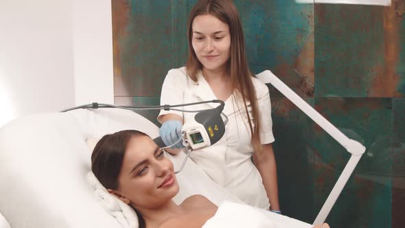 Cosmetologist Using Laser Apparat on Woman Face at Beauty Clinic alt